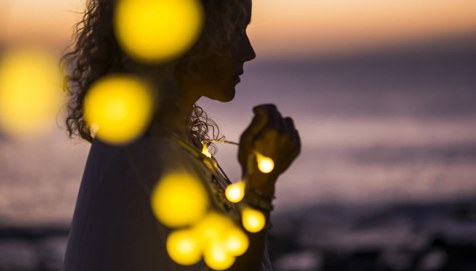 Silhouette einer Frau mit Lichterkette am Strand bei Sonnenuntergang