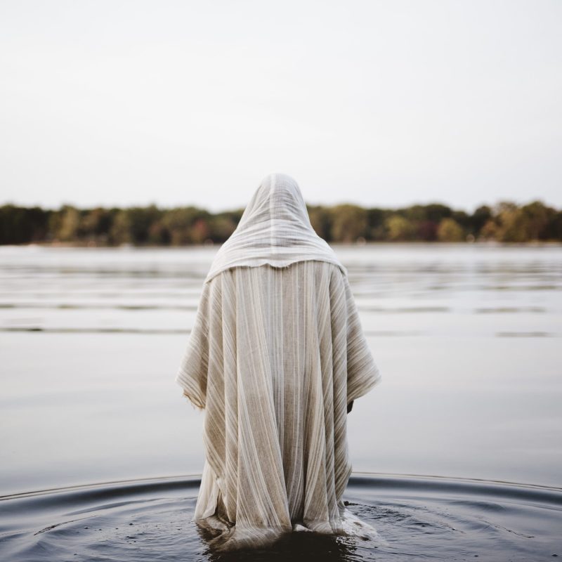 A person wearing a biblical robe walking in the water with a blurred background shot from behind