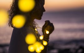 Beautiful woman in the shadow with yello bulb lights - coloured sunset in background - magic and emotional lifestyle concept - dreaming and hope - prayer for the world