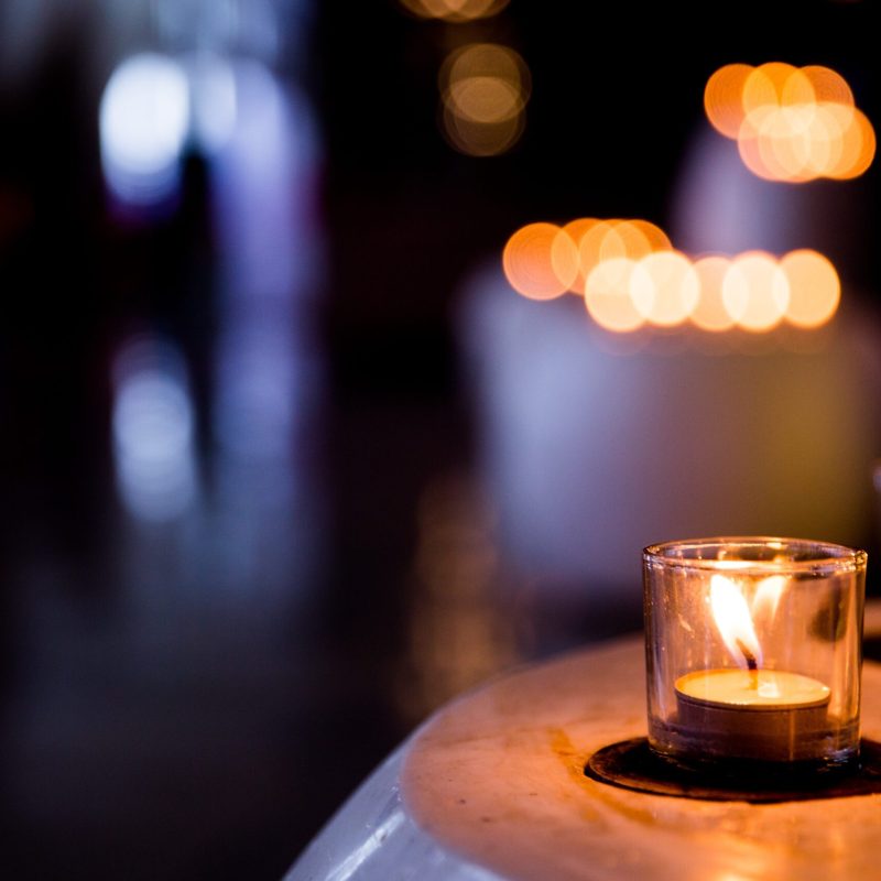 Flame of many candles burning on blurred lights background. Holiday concept.