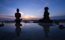 A woman's silhouette next to stacked rocks against the background of the sky at sunset.