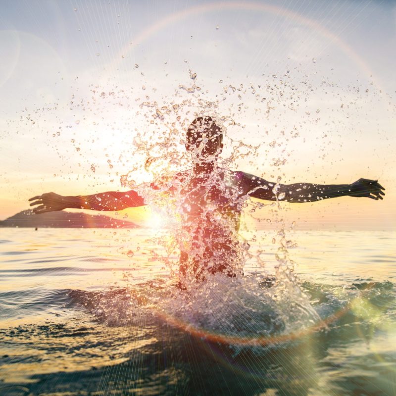 Man splashing water during summer holidays - Young attractive man having fun on a tropical beach at sunset